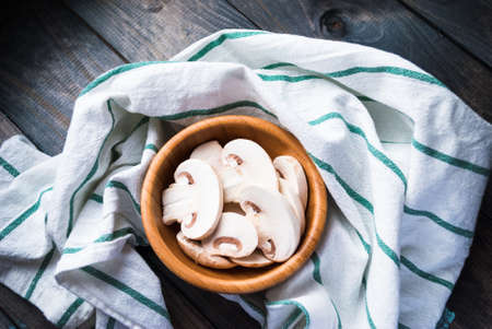 Sliced raw white champignon mushrooms, bamboo bowl, green striped kitchen towel, top view, horizontalの写真素材