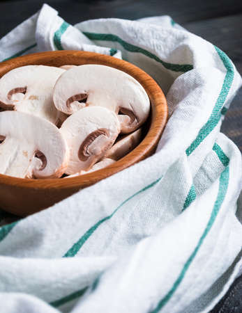 Sliced raw white champignon mushrooms, bamboo bowl, green striped kitchen towelの写真素材