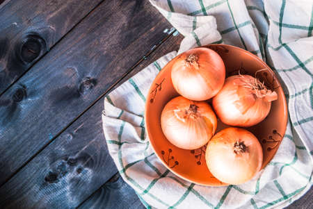 Raw onion in a ceramic brown bowl on a kitchen table. Top view