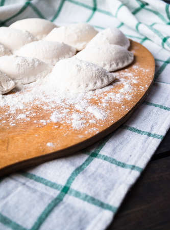 Raw dumplings sprinkled with flour on a cutting board and a striped towel. Close upの写真素材