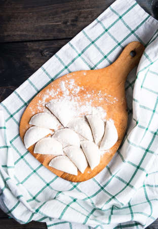 Raw dumplings sprinkled with flour on a cutting board and a striped towel. Top viewの写真素材