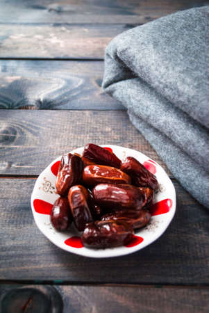 Saucer of date fruits and folded grey blanket on a wooden backgroundの写真素材