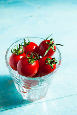 Ripe red cherry tomatoes in a glass on a turquoise background, top viewの写真素材