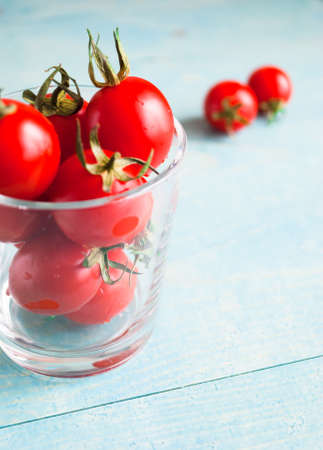 Ripe red cherry tomatoes in a glass and a couple of it on a turquoise wooden surface, close upの写真素材