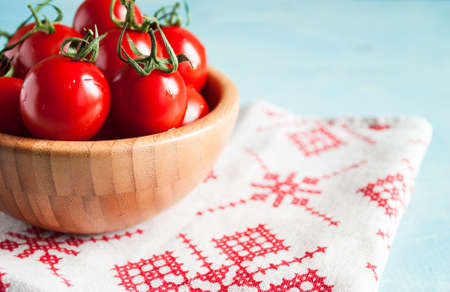 Ripe red cherry tomatoes in a bowl on a white kitchen towel with red patternの写真素材