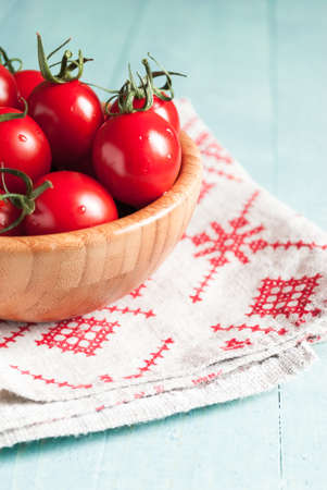 Ripe red cherry tomatoes in a bowl on a white kitchen towel with red patternの写真素材
