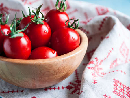 Ripe red cherry tomatoes in a bowl on a white kitchen towel with red patternの写真素材