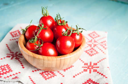Ripe red cherry tomatoes in a bowl on a white kitchen towel with red patternの写真素材