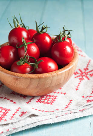 Ripe red cherry tomatoes in a bowl on a white kitchen towel with red patternの写真素材
