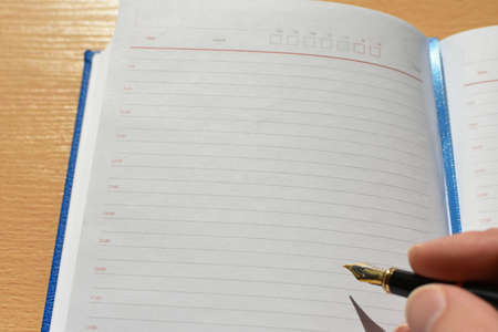 Hand writes pen in a notebook on a wooden desktop in the office, copy spaceの写真素材