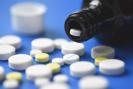 Tablet fell from the bottle to the blue medical table, white and yellow tablets scattered on the...