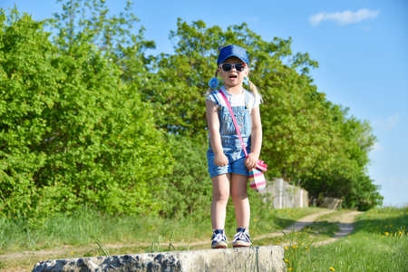 A little girl is standing on an old concrete block, crying, afraid of heights, fear. Little girl enjoying nature. Outdoor playingの写真素材