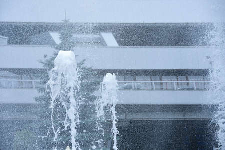 Splashes from the fountain fly against the background of modern building made of metal in hot weatherの写真素材