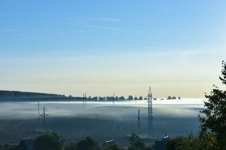 Summer misty morning. The road is in the park. Sunrise over the forest behind thick fogの写真素材