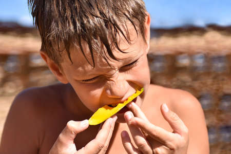 Teenager eating juicy fruit is the mango on the beach, close up