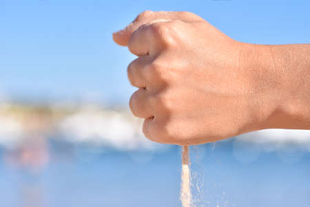 Sea sand pouring out of children hands on the beach, close up