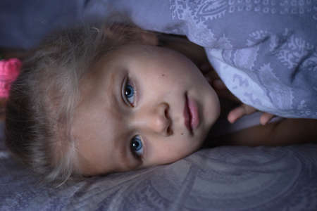 Little girl is sick and basks under the covers in bed