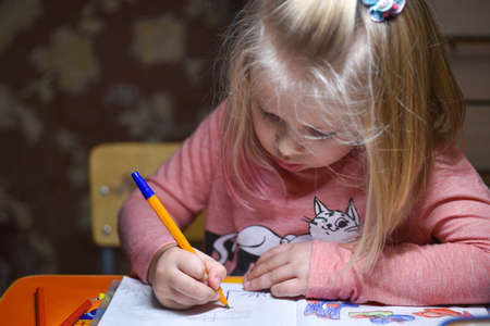 Child preschooler learns to draw and write in notebooks at home in the evening under the light from...