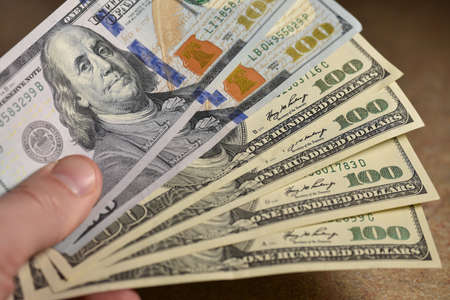 Hand holding hundred dollar bills.