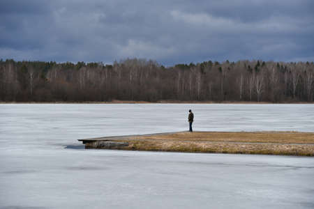 A lone man on the island looks at the frozen lake.