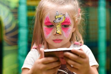 A little girl with a pattern of a unicorn on her face looks in the mirror.の写真素材