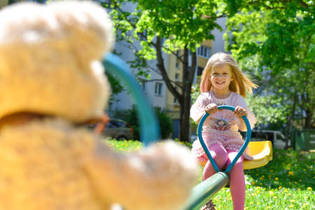 Cheerful girl riding on a swing with a toy bear.の写真素材