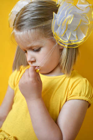 Portrait of a sad shy little girl in a yellow dress on a yellowの写真素材