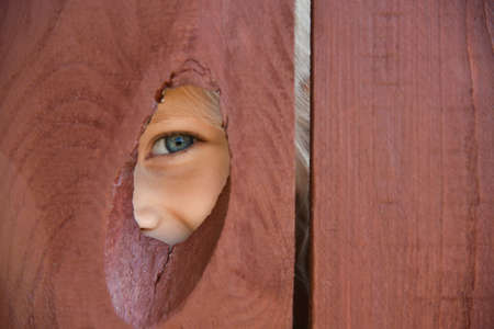 The eye of the girl looks through a hole in the fence.
