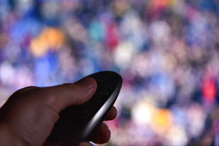 Male hand switches channels on tv remote at night.