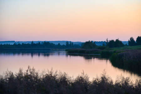 Lake with reeds at sunset in a haze, lonely boat.の写真素材