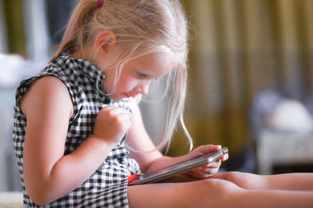 Child girl in a dress sitting watching a video and playing on a smartphone.