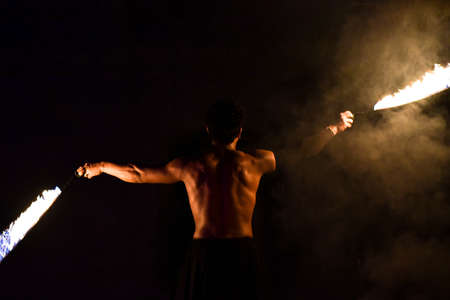 Fakir juggles fire on a black background.