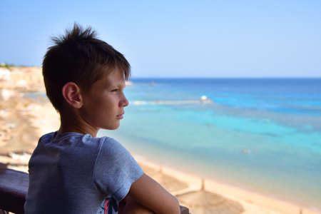 A teenager looks at a sunny sea beach and is sad.