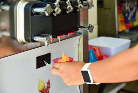 Girl hand takes ice cream into a cup from the machine.の写真素材