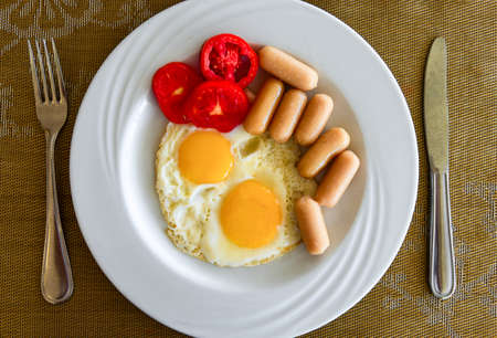 Fried eggs with sausages and tomatoes on a white plate.の写真素材