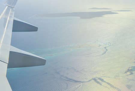 Wing of a passenger plane on the background of an island in the sea.