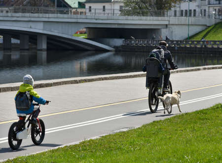 Family with dog riding a bicycle on a bike path in the city.