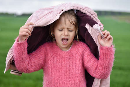Girl hides her head under a jacket in the rain.の写真素材