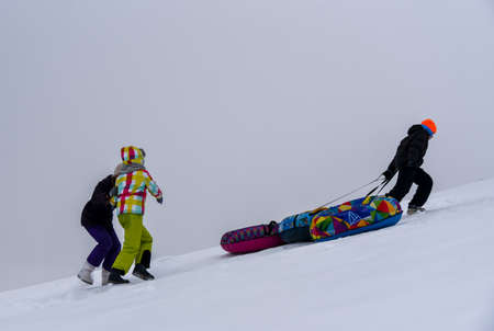 Teen helps friends pull tubing down a snow slide.