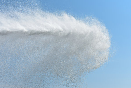 Powerful jet of water from the fire hose of the car against the background of the blue sky.