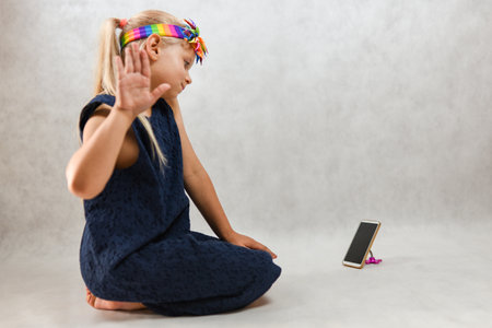 Child in a blue dress posing in front of a smartphone.