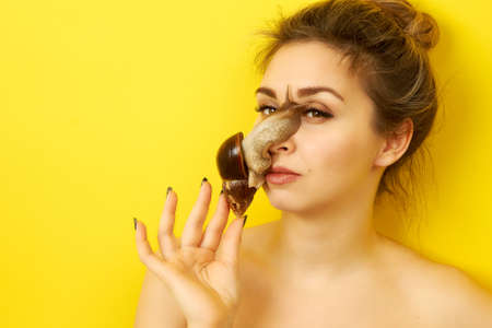 Cheerful young woman with a snail on her face on a yellow backgroundの写真素材