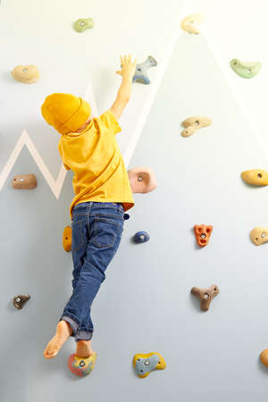 A boy of 3-4 years old tries to climb up the climbing wall trying to reach the sun. Striving for high goalsの写真素材