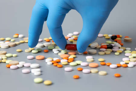 A hand in a blue glove selects pills on a gray background. The concept of the problem of correct...