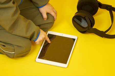 Close-up of a boy with wireless headphones, who plays online games on a digital tablet, communicates with friends, and studies online.の写真素材