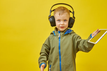 A boy wearing wireless headphones with a digital tablet on a yellow background. Modern children and...