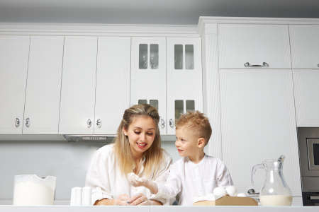 Happy mom and baby cook in a white kitchen at a table made of dough, they are very good and fun togetherの写真素材