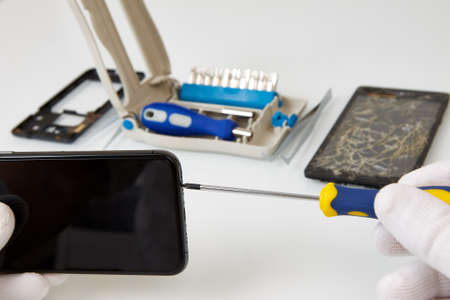 Disassembled smartphone and tools for its repair: tweezers and screwdrivers. The process describing...