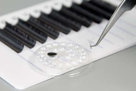 A tablet with false eyelashes, glue and tweezers on a gray background. Cosmetic accessories for...