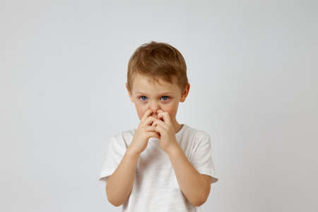 A small preschool boy picks his nose with two fingers on a white background. Bad habitの写真素材